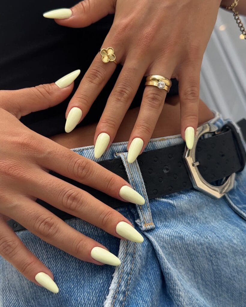 summer nail colors, pale lemon glossy almond nails with gold rings and denim