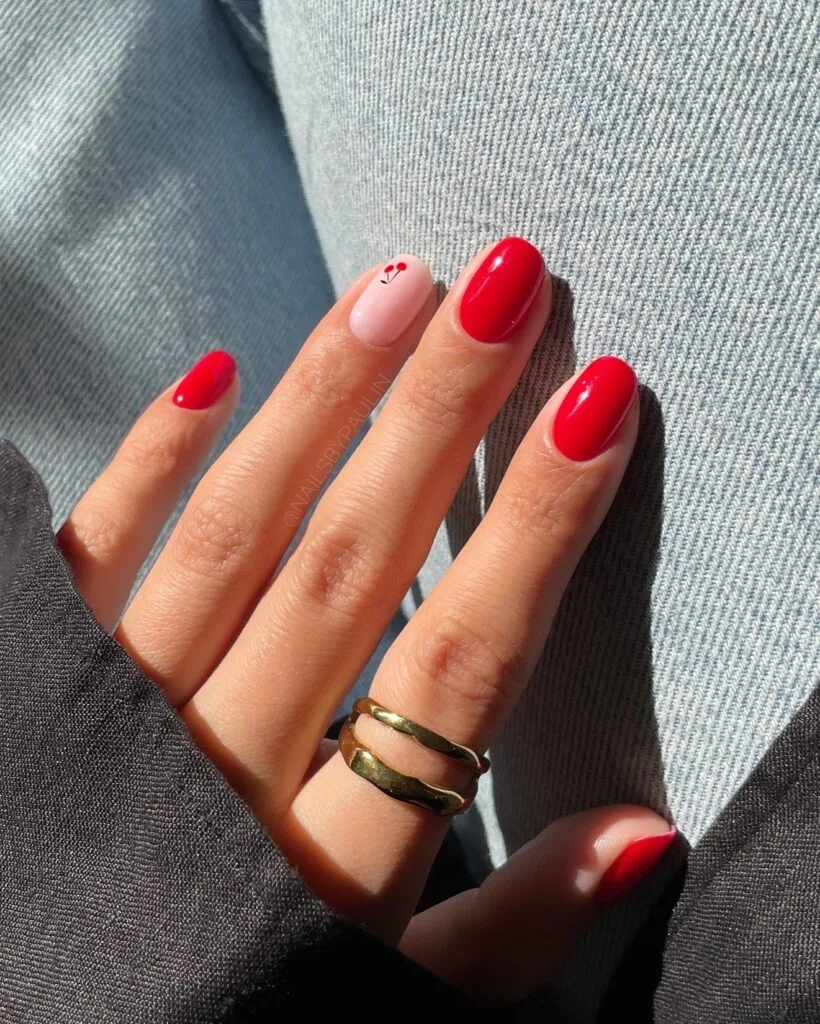 july nail colors, glossy cherry red round nails with soft pink accent nail and tiny cherry art