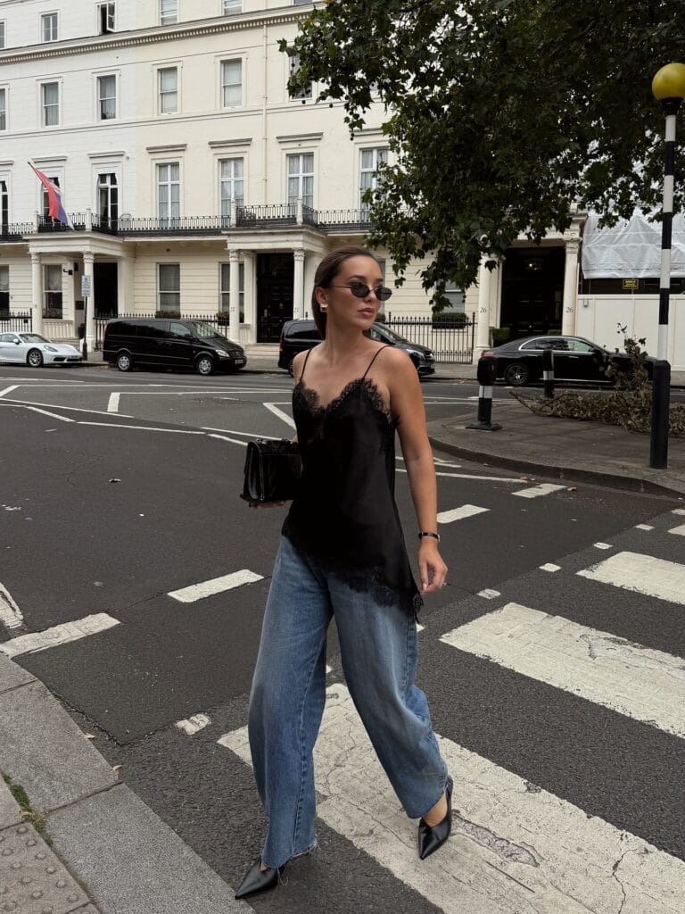 July outfit with black lace-trim cami, light wash wide-leg jeans, black pointed slingbacks, and quilted bag
