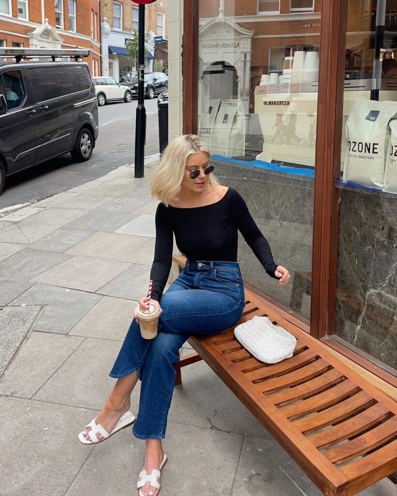July outfit with black long-sleeve boat-neck top, cropped jeans, white slide sandals, and white woven clutch
