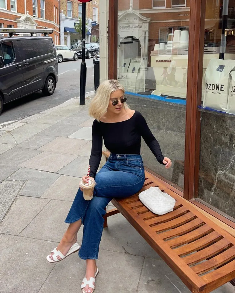 July outfit with black long-sleeve boat-neck top, cropped jeans, white slide sandals, and white woven clutch
