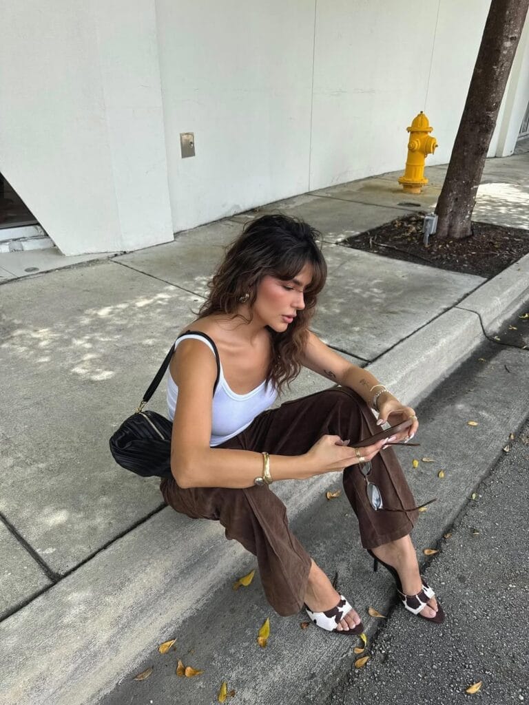 July outfit with white scoop tank, brown wide-leg trousers, cow print heeled sandals, and black shoulder bag
