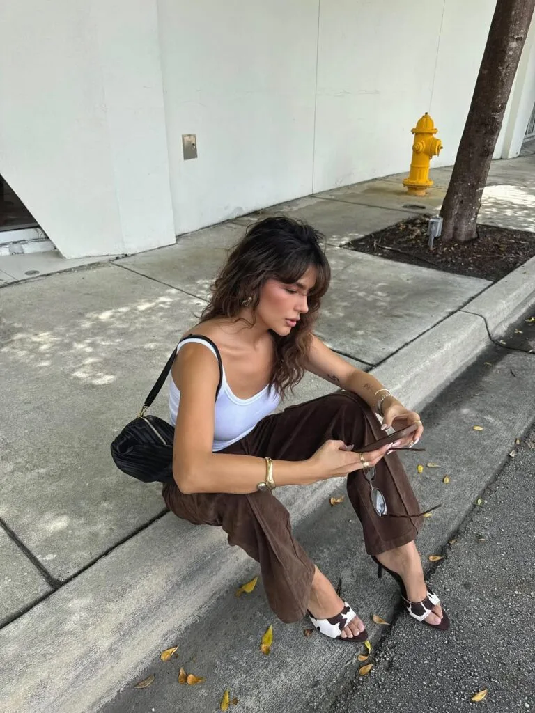 July outfit with white scoop tank, brown wide-leg trousers, cow print heeled sandals, and black shoulder bag
