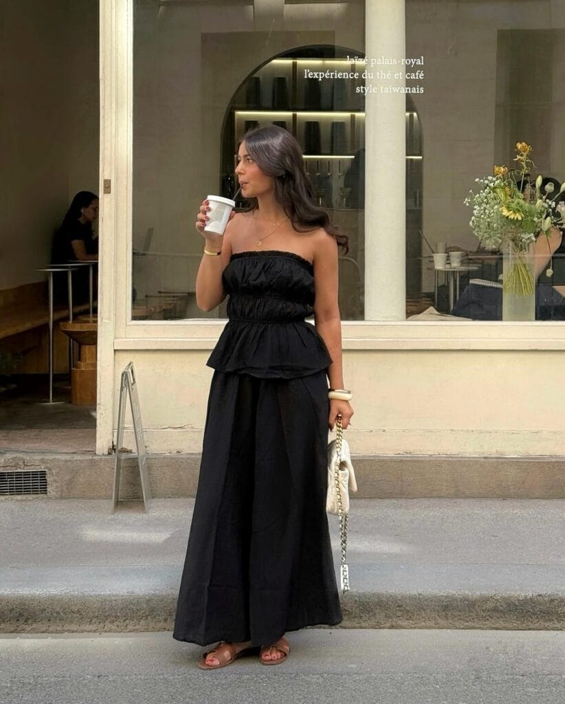 summer outfit with black strapless ruched top, flowy black maxi skirt, tan slide sandals, and white chain bag
