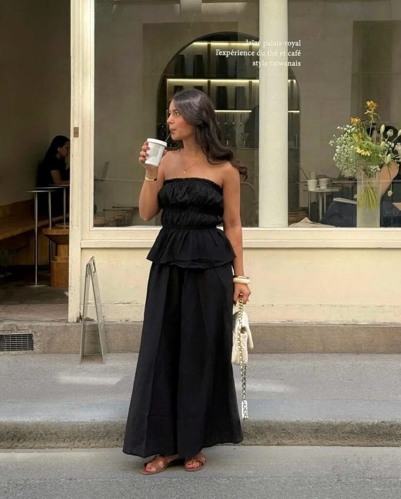summer outfit with black strapless ruched top, flowy black maxi skirt, tan slide sandals, and white chain bag
