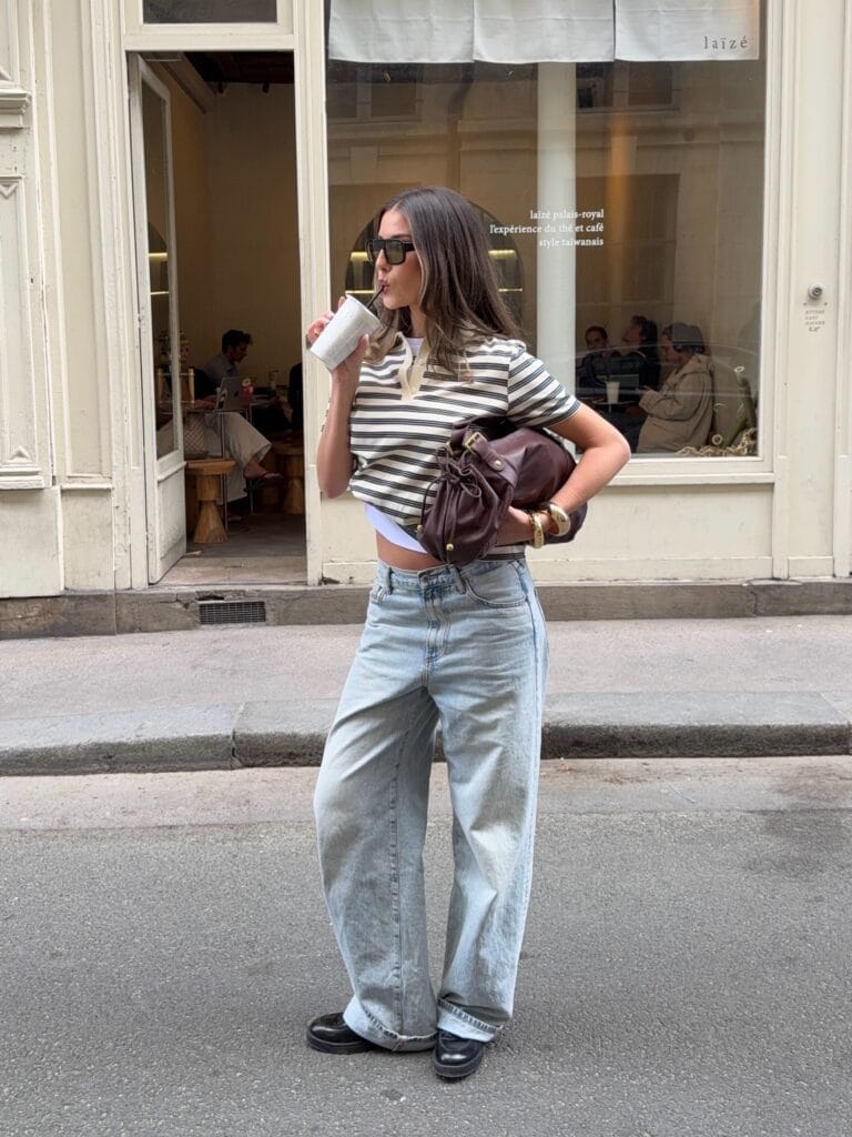  July outfit with striped polo tee, baggy light wash jeans, chunky black loafers, and brown leather bag
