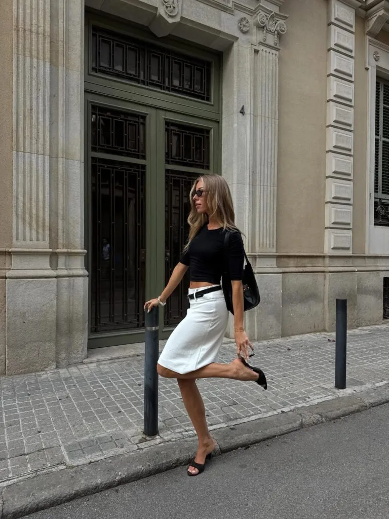 July outfit with fitted black tee, low-rise white knee-length skirt, black belt, and heeled mules
