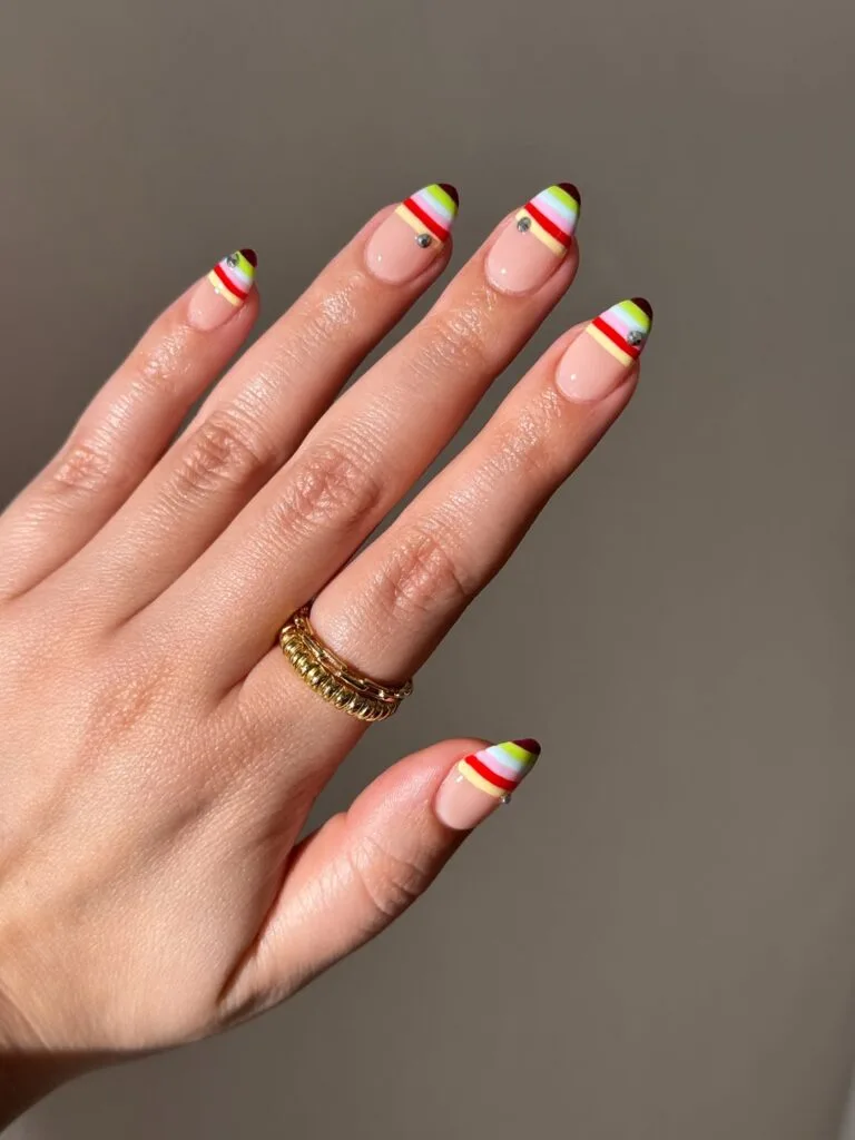 summer nails, almond nude nails with multicolor striped French tips and tiny gem accents
