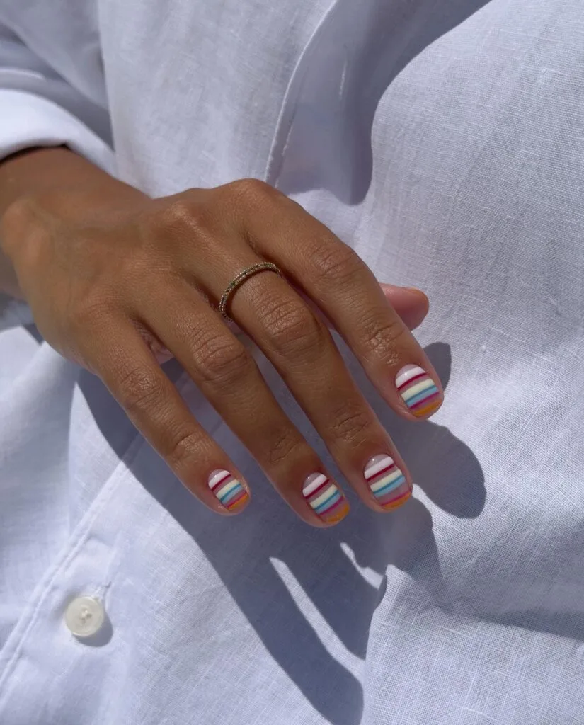 august nails, short nails with thin white, cherry, blue, and orange horizontal stripes on sheer base
