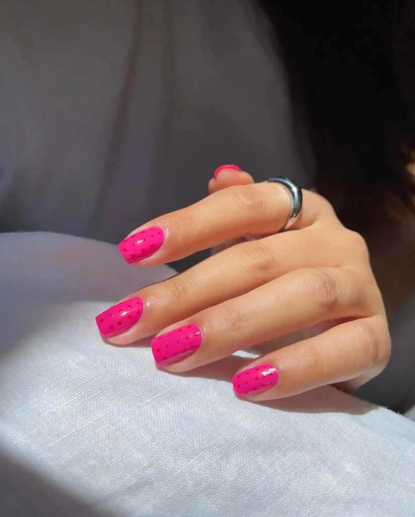 august nails, short square hot pink nails with tiny red polka dots
