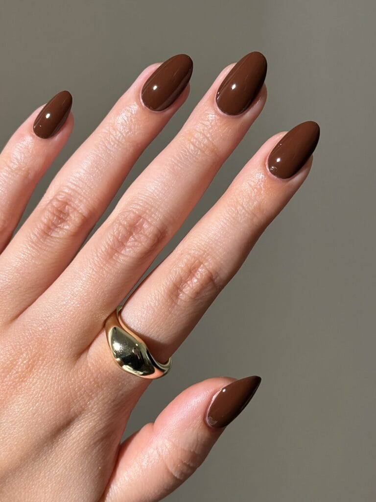 Glossy espresso brown almond nails in sunlight with a gold ring, a fall nail colors look.