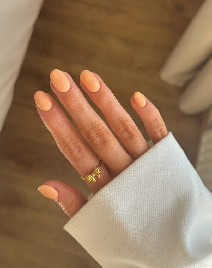 Glossy golden apricot nails on a soft oval shape in warm light, a September nails color idea.