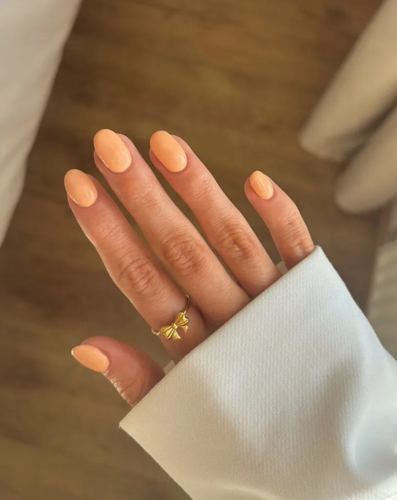 Glossy golden apricot nails on a soft oval shape in warm light, a September nails color idea.