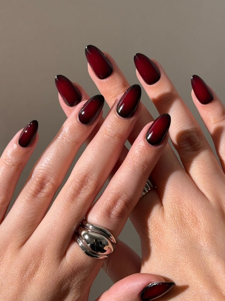 Black cherry fall aura nails with bright red centers, dark edges, and glossy almond shapes.
