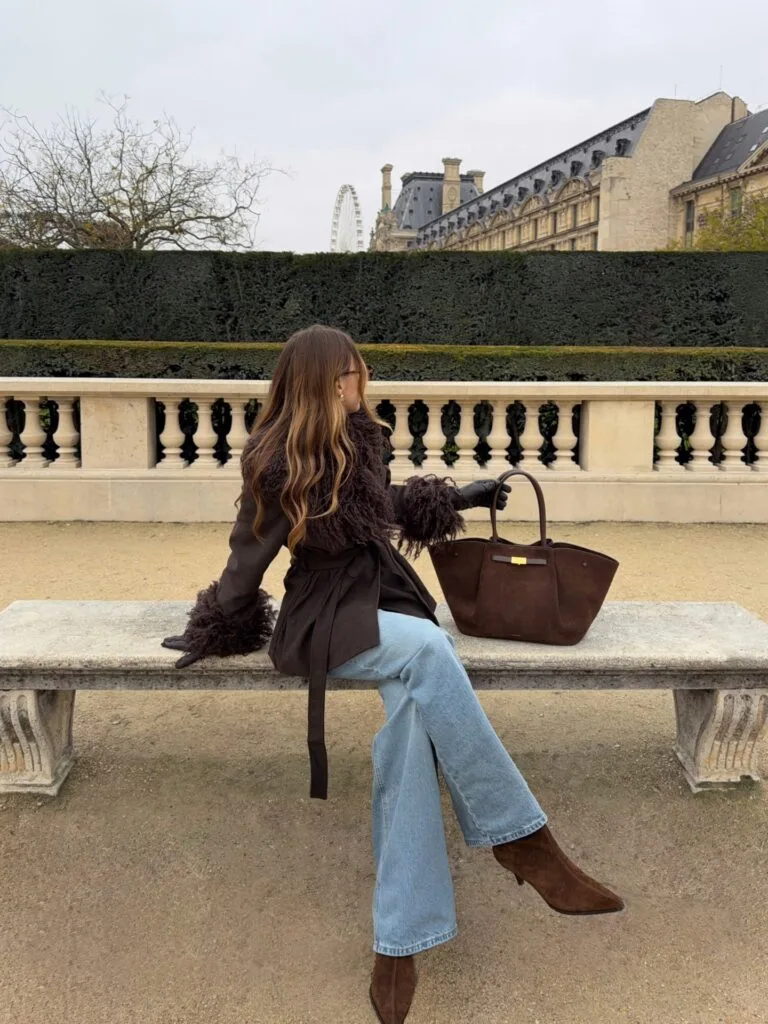 Woman in a brown textured jacket with shaggy trim, jeans, and suede boots in a fall outfit.