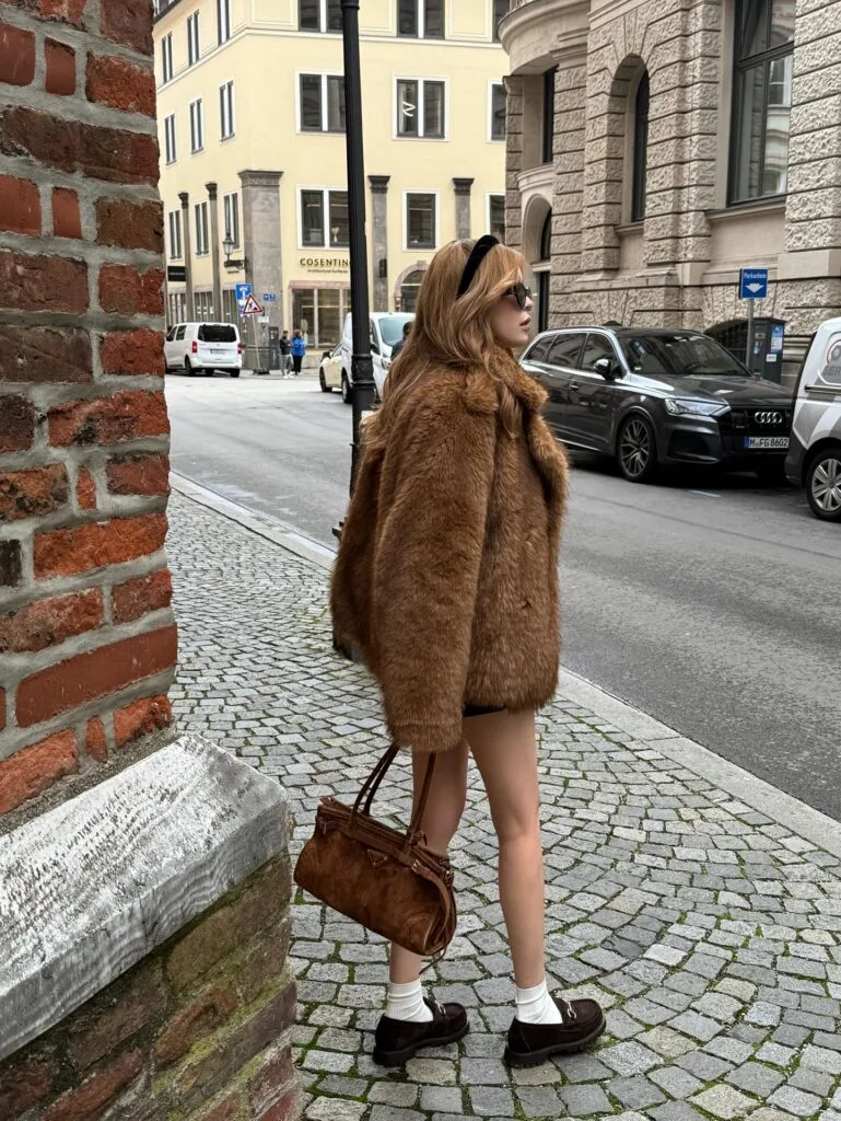 Woman in a plush brown coat with loafers and white socks in a fall 2026 outfit.