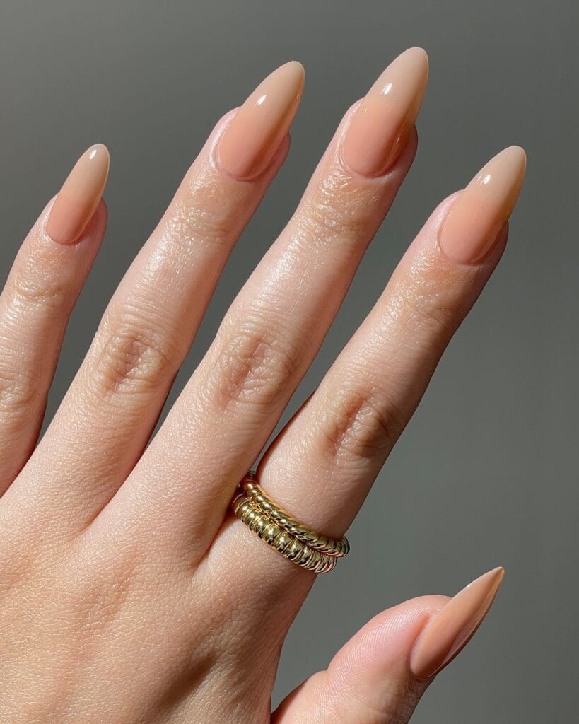 Glossy almond nude nails in a warm peach-beige shade.

