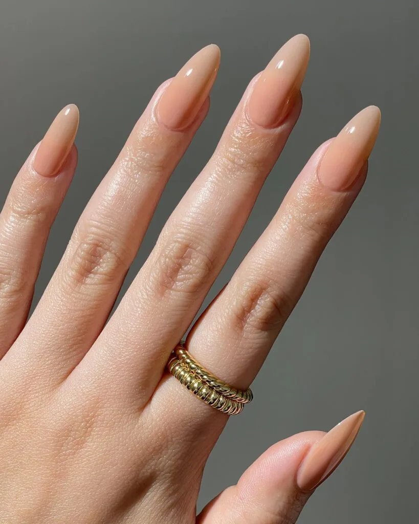 Glossy almond nude nails in a warm peach-beige shade.