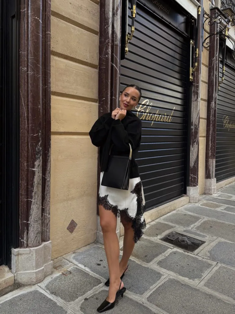 Early fall outfit with black sweater, white lace-trim skirt, black slingback heels, and black shoulder bag.