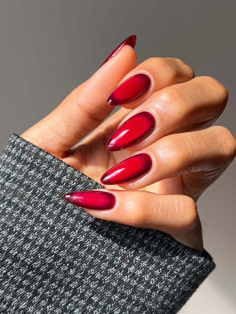 Crimson fall aura nails with bright red centers, deep wine edges, and glossy almond shapes.
