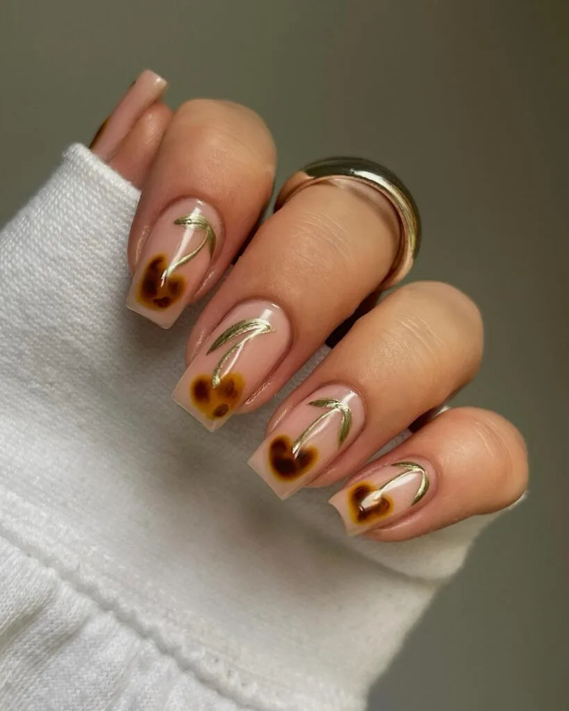 Square nude nails with tortoiseshell cherry art and delicate metallic gold stems.

