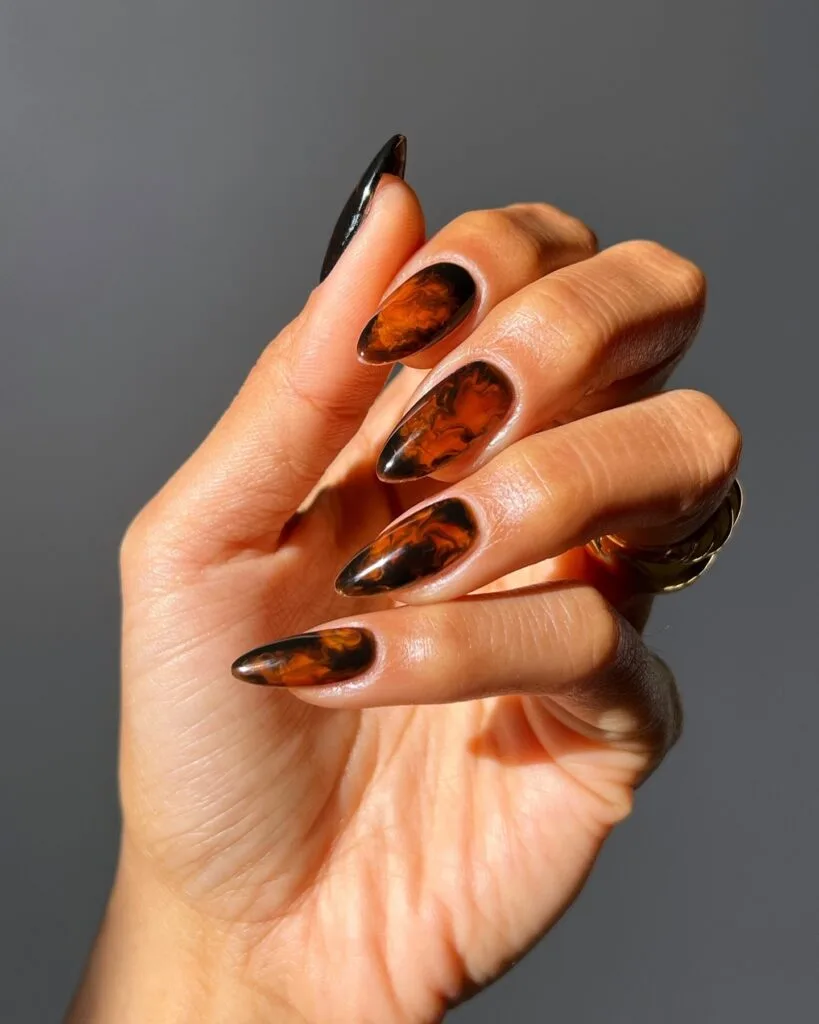 Long almond tortoiseshell nails with smoky burnt-amber swirls and deep brown edges.
