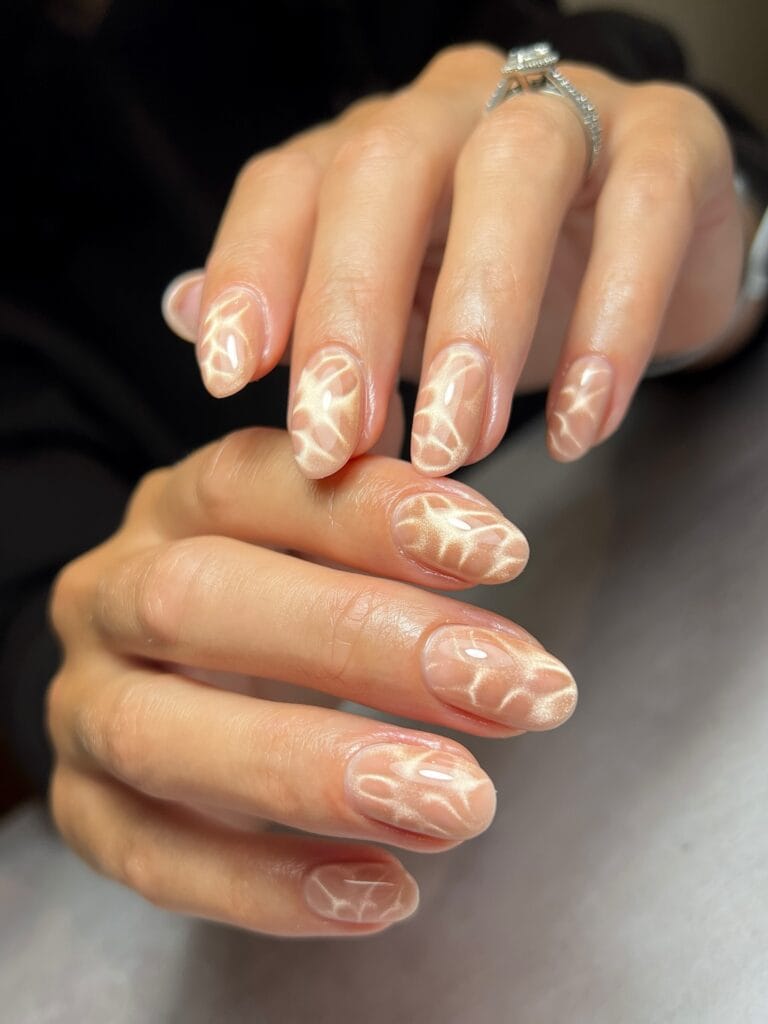 Nude autumn nails with champagne cat-eye shimmer forming soft curved patterns.