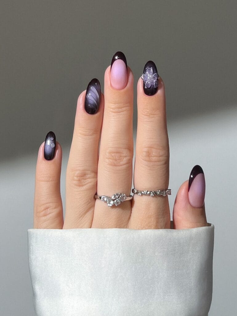 Dark plum autumn nails with lavender aura accents, French tips, pearls, and a translucent flower.
