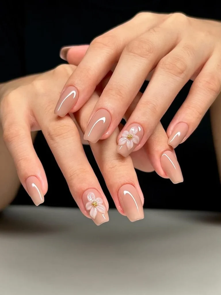 Square nude nails with white curved lines, raised floral accents, and tiny gold centers.
