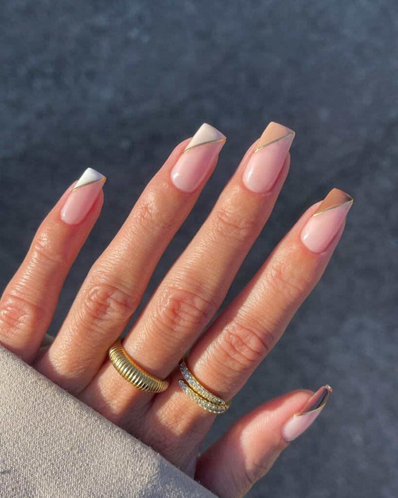 Nude nails with diagonal cream and taupe French tips outlined in thin gold.
