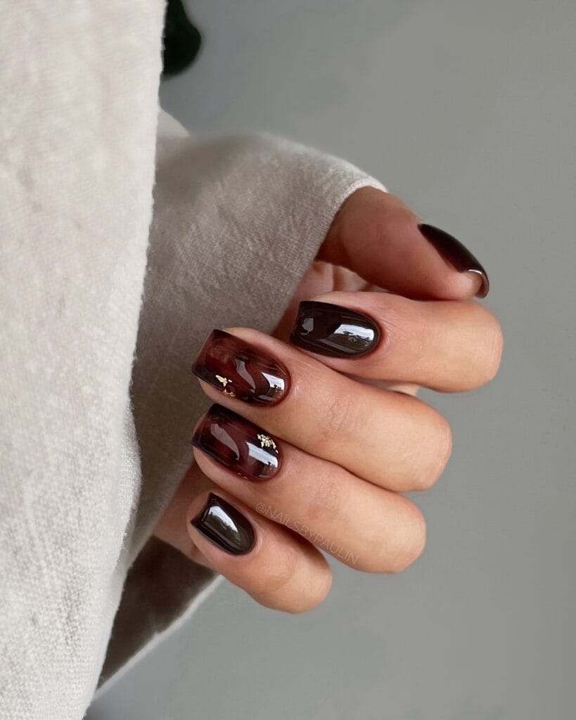 Short square tortoise shell nails in translucent burgundy with dark brown and small gold foil accents.
