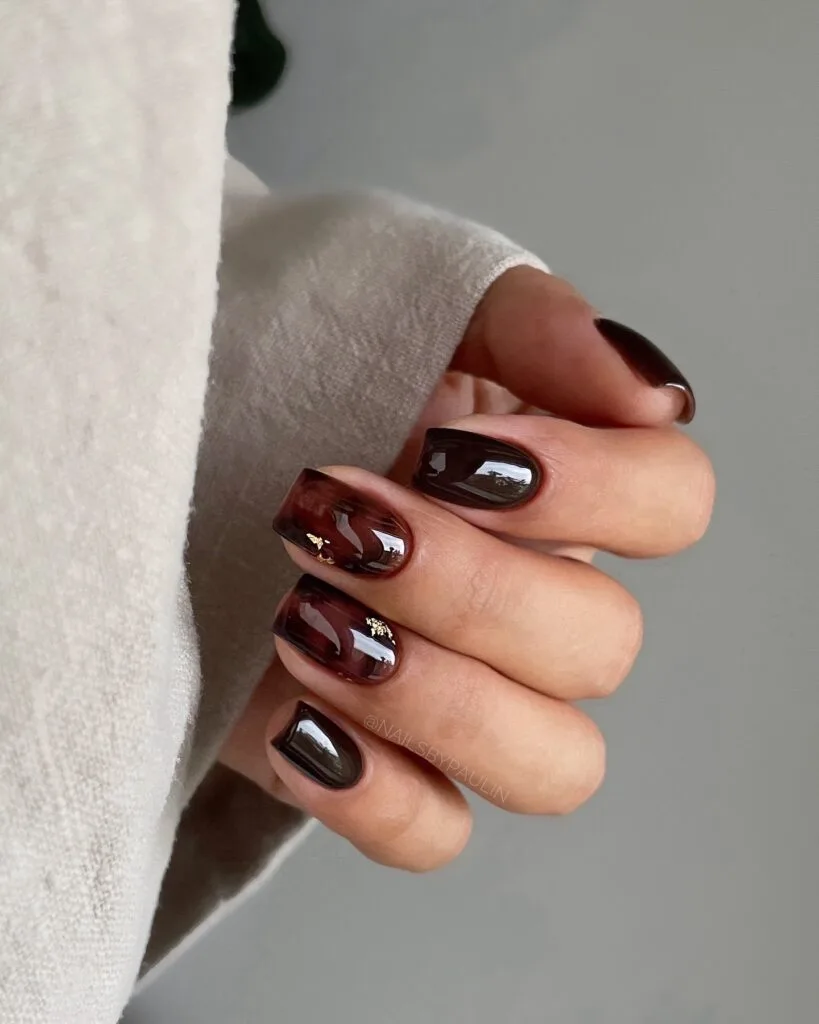 Short square tortoise shell nails in translucent burgundy with dark brown and small gold foil accents.
