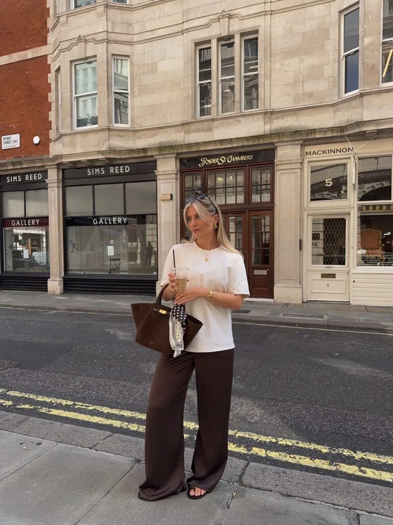 Early fall outfit with a white tee, chocolate satin wide-leg pants, brown tote bag, and sandals.