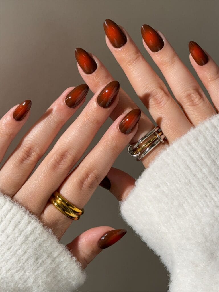 Burnt orange autumn nails with warm brown aura edges and a high-gloss almond finish.
