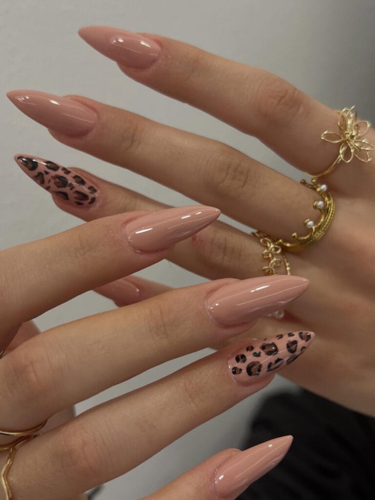 Glossy almond nude nails with two black and brown leopard print accents.
