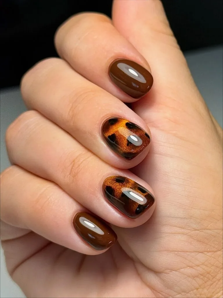 Short tortoiseshell nails with copper shimmer, dark patches and glossy chocolate brown accent nails.
