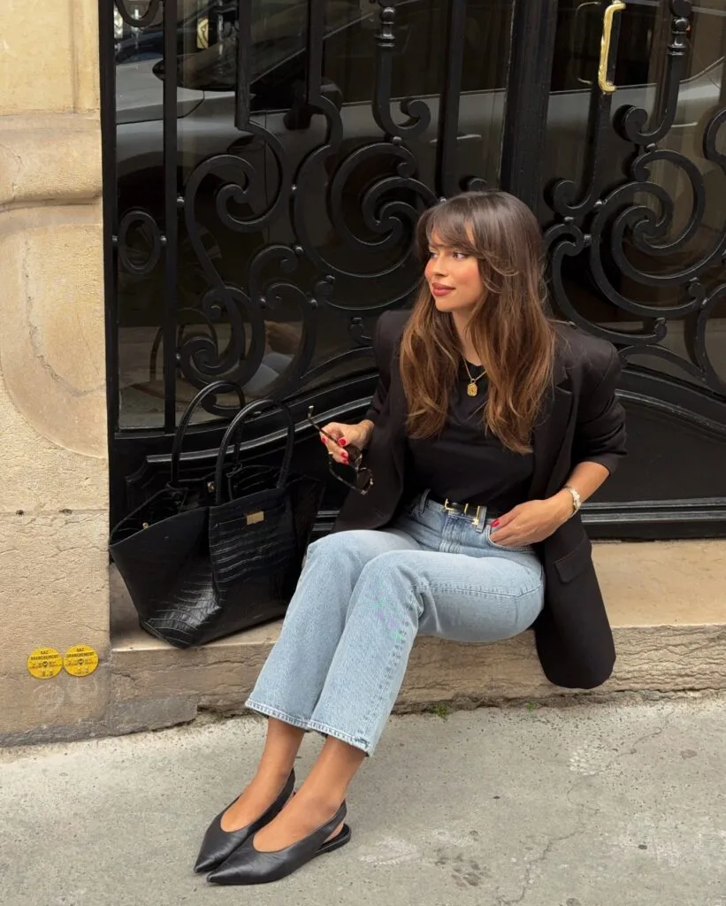 Autumn outfit with black blazer, black top, straight-leg jeans, pointed black flats, and black tote bag.
