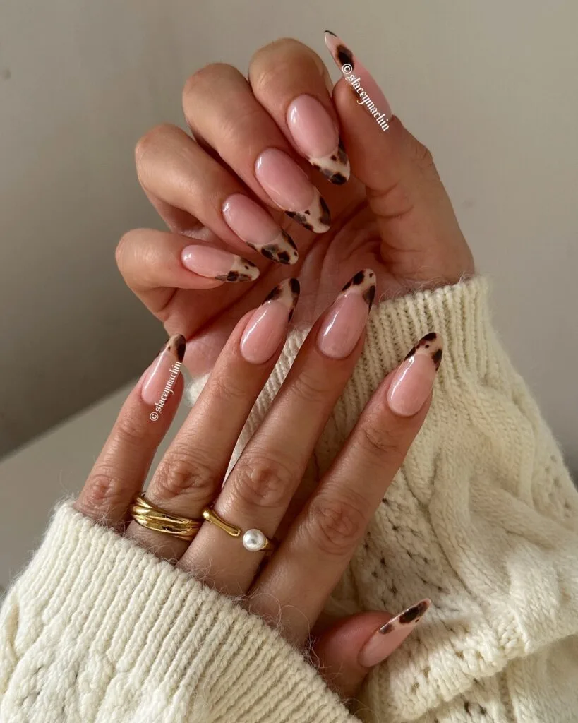 Sheer pink almond nails with soft beige tortoiseshell French tips and dark brown spots.
