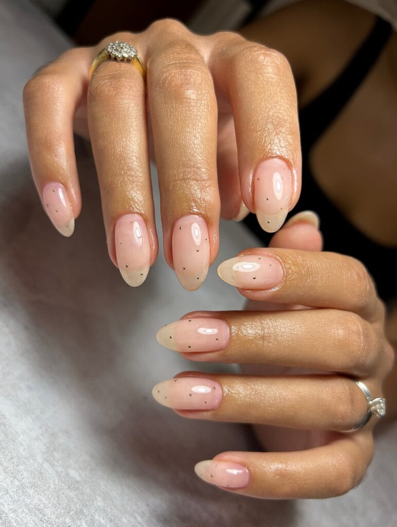 Milky pink autumn nails with a glossy finish and tiny scattered gold dot accents.