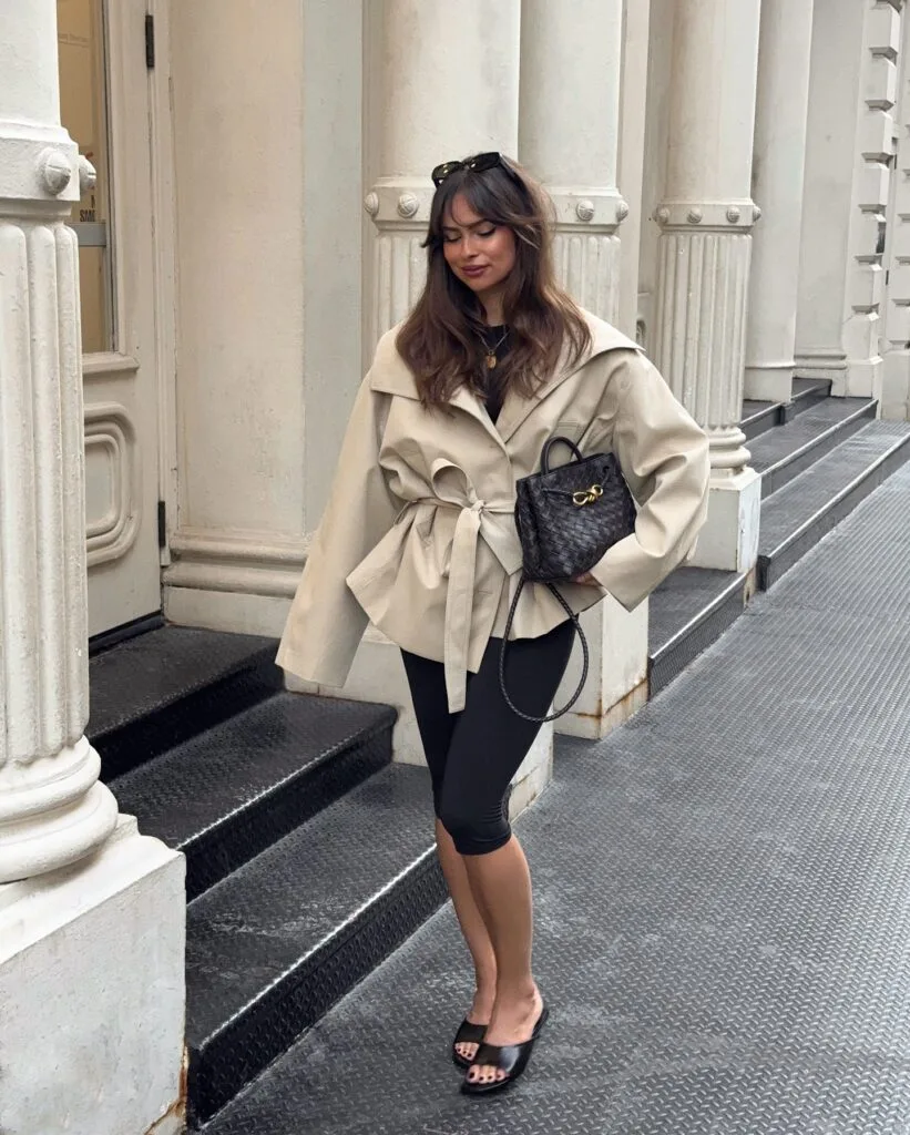 Early fall outfit idea with beige wrap jacket, black capri leggings, black slides, and woven black bag.