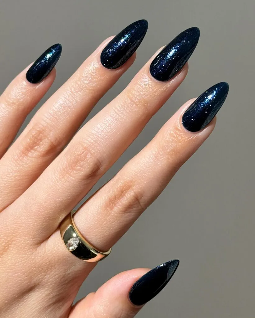 Shimmery midnight blue almond nails with fine sparkle and a gold ring, an autumn nails idea.