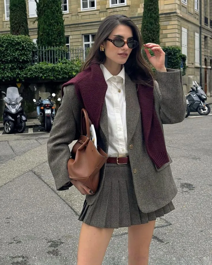 Woman in a grey pleated skirt suit, white shirt, and burgundy knit for a fall outfit.