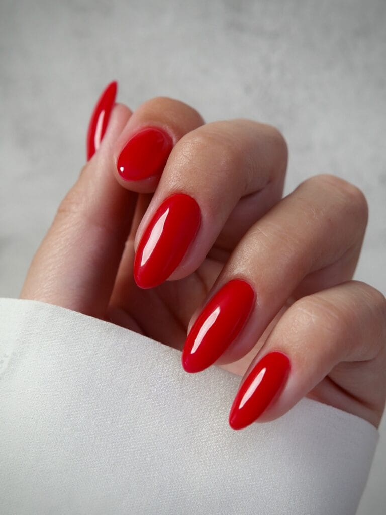 Long almond nails in bright tomato red with a glassy finish, an autumn nail colors idea.