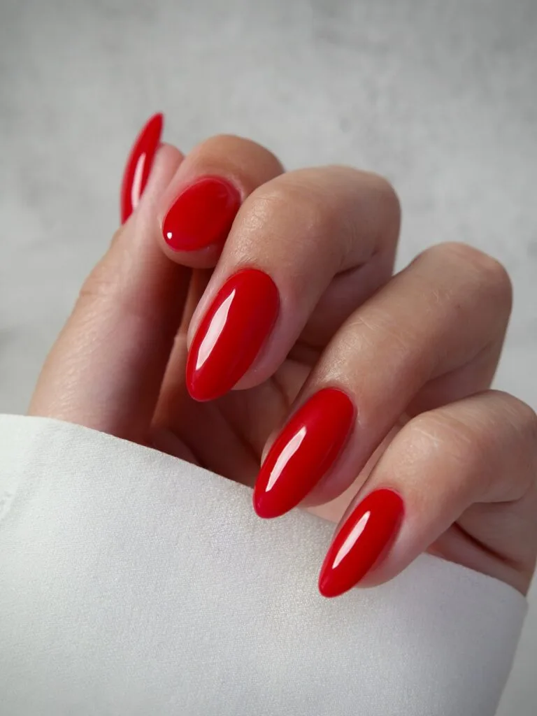 Long almond nails in bright tomato red with a glassy finish, an autumn nail colors idea.