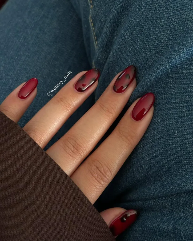 Red tortoise shell nails with translucent cherry polish, smoky dark patches and solid burgundy nails.
