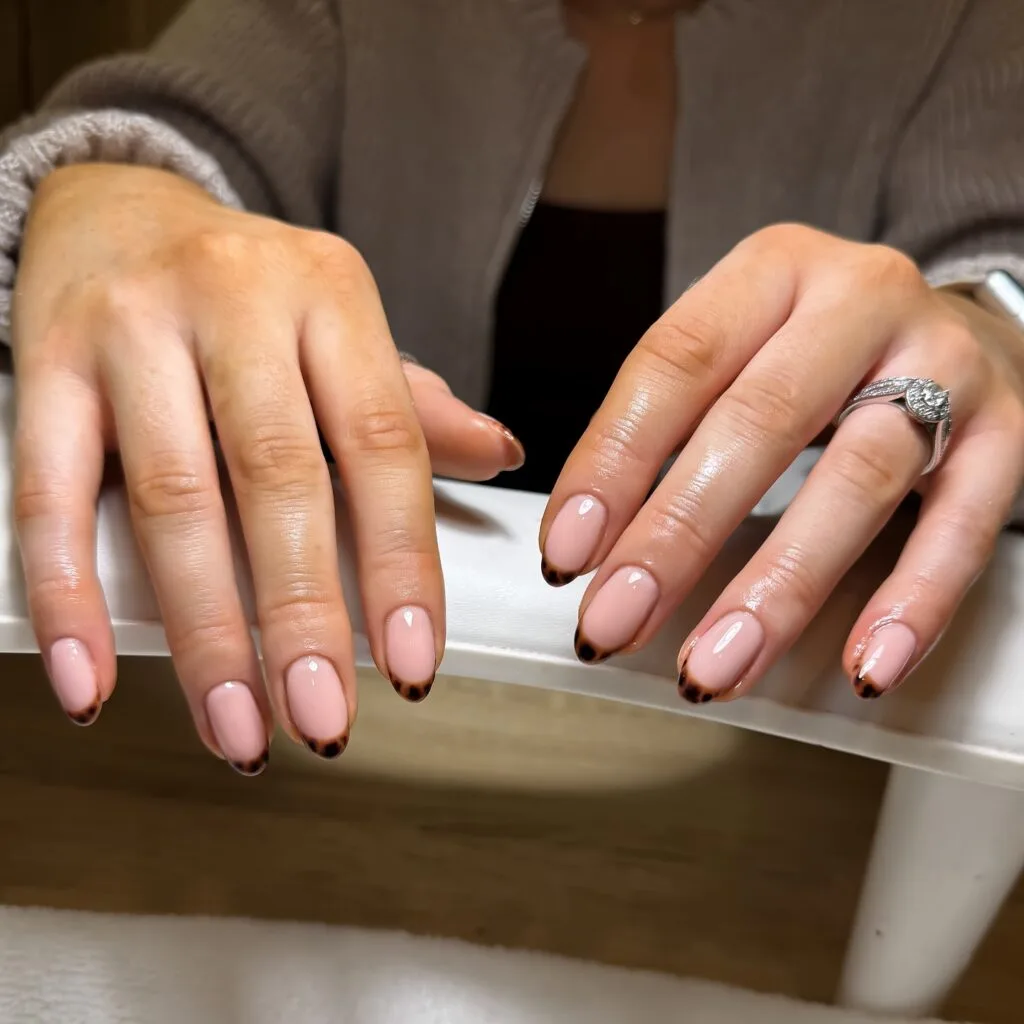 Sheer pink almond nails with thin tortoiseshell French tips in amber and dark brown.
