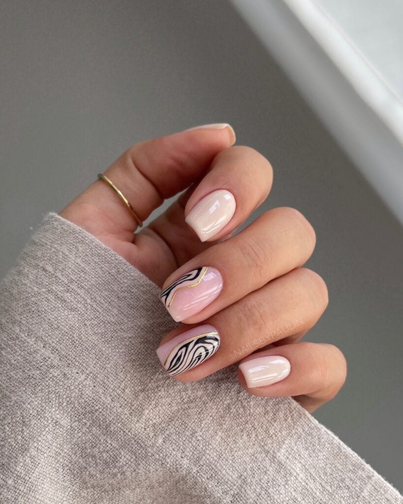 Short nude nails with black swirl art, thin gold lines, and visible text “@NAILSBYPAULIN.”
