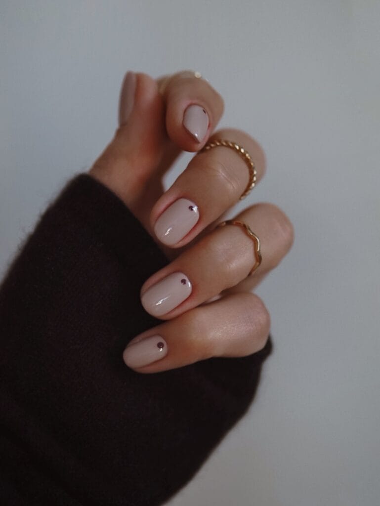Short creamy nude nails with one tiny burgundy dot on each nail.
