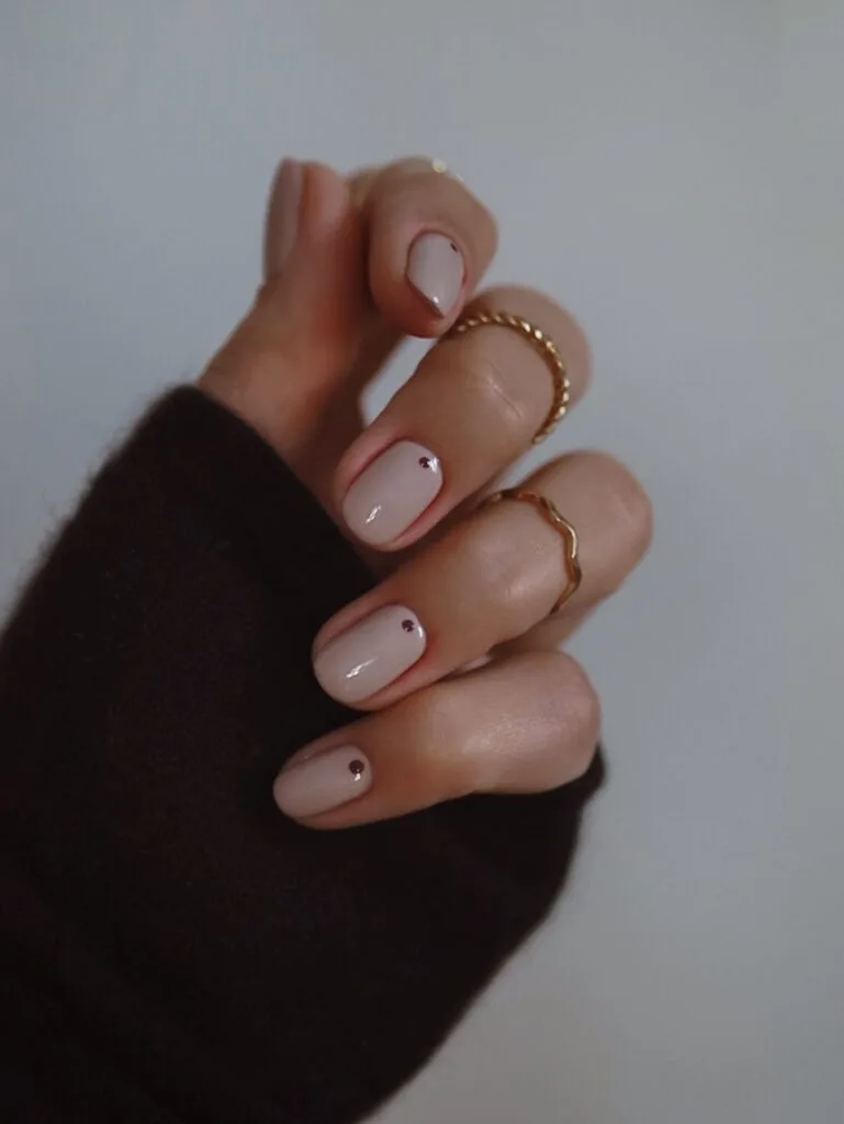 Short creamy nude nails with one tiny burgundy dot on each nail.