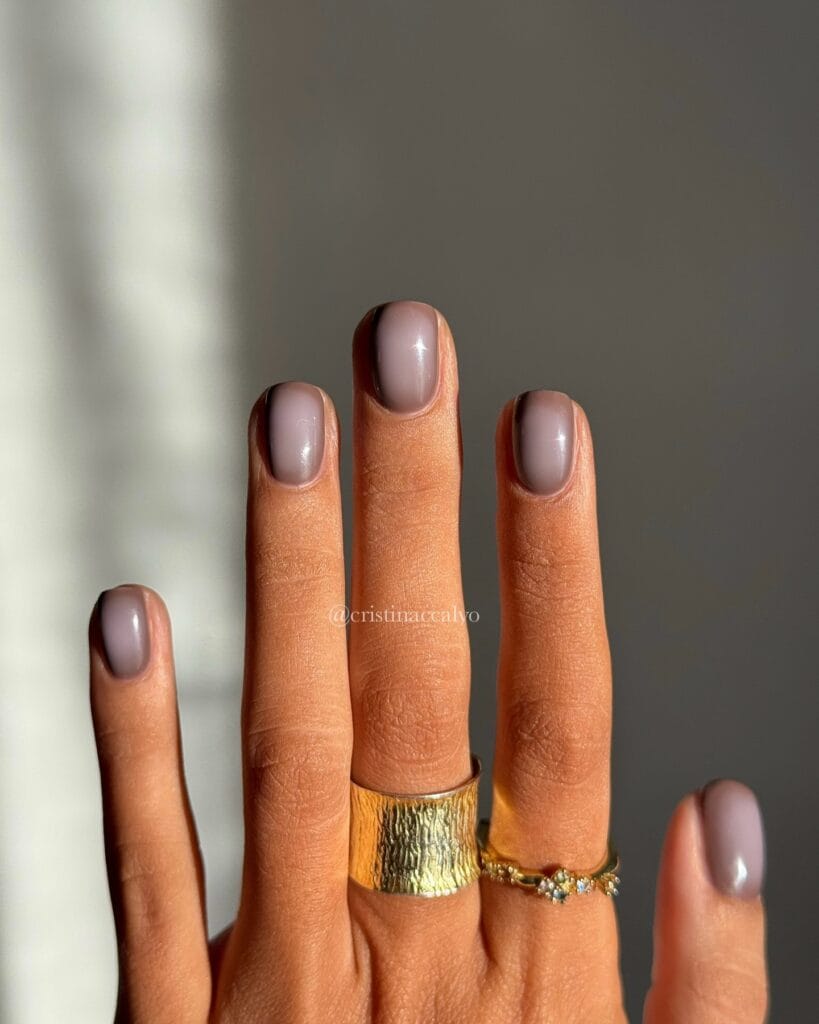 Short taupe fall aura nails with soft dark shading and text “@cristinaccalvo.”
